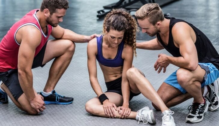 Young woman injured at the gym with two male personal trainers helping her