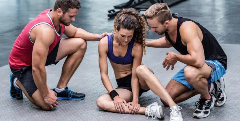 Young woman injured at the gym with two male personal trainers helping her