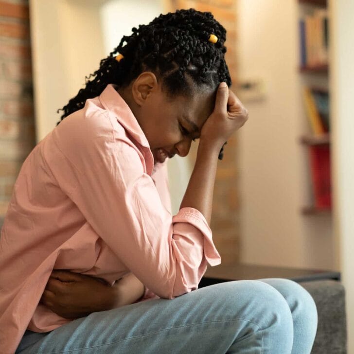 African american woman suffering from PMS and menstruation pain, having stomach ache, sitting on