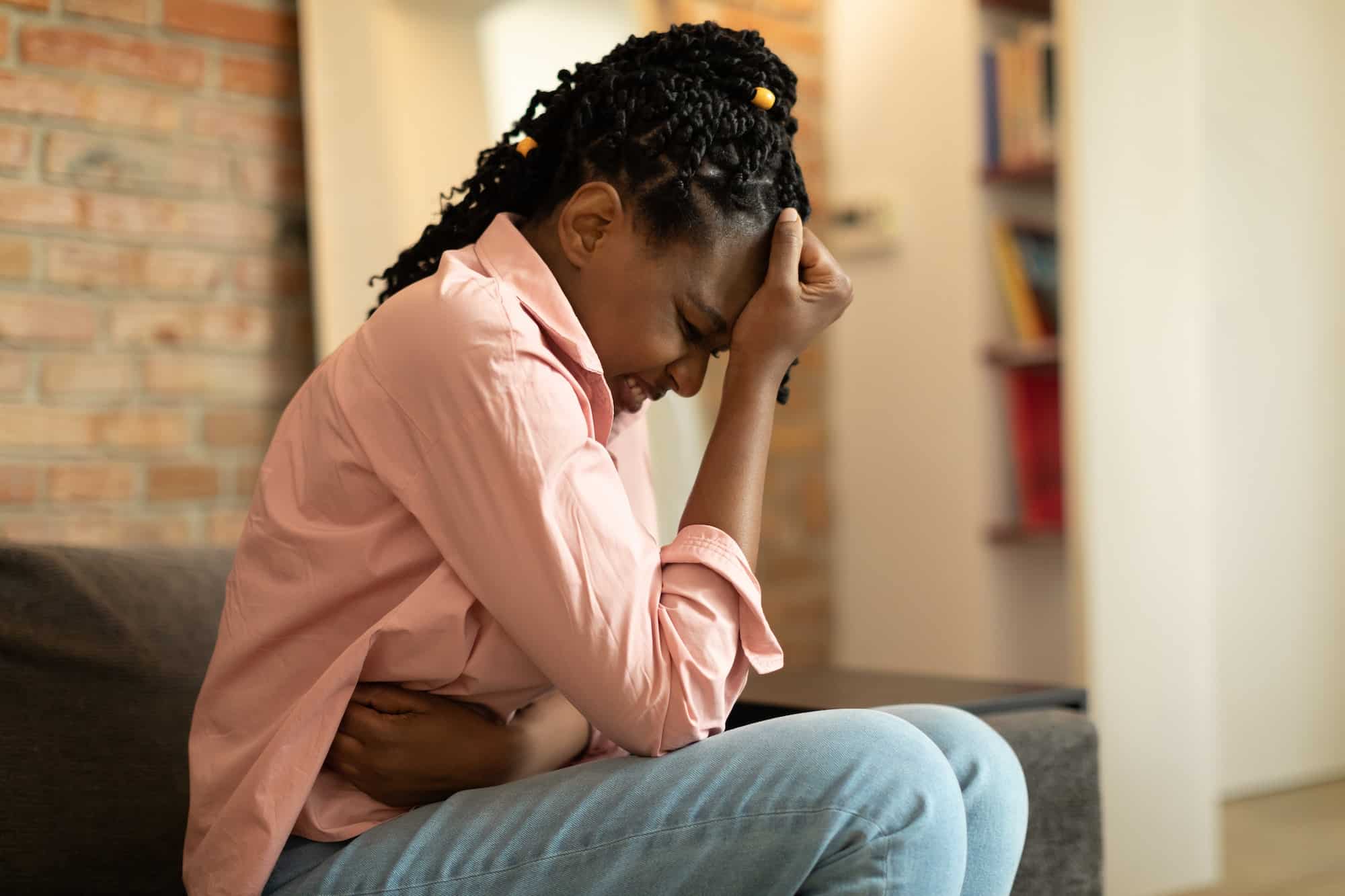African american woman suffering from PMS and menstruation pain, having stomach ache, sitting on