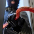 Bandit in balaclava holding a crowbar to break a glass window.