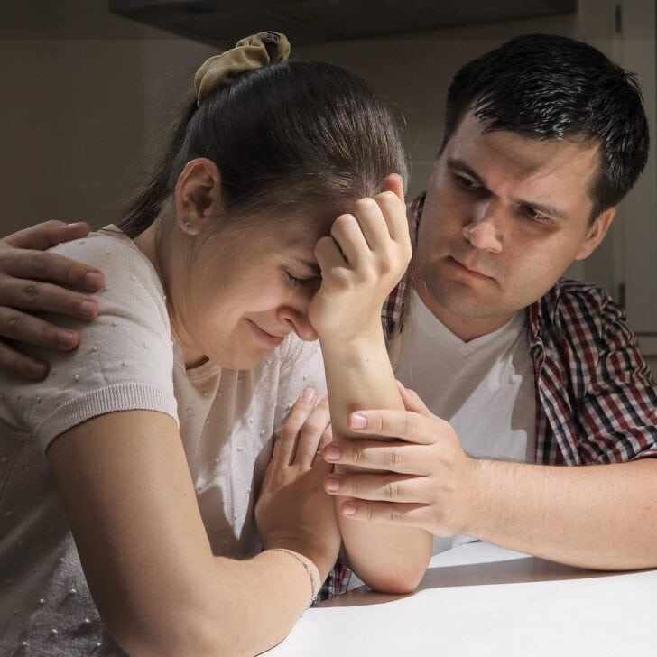 Young man consoling and hugging his crying wife on kitchen at night. Concept of despair, stress