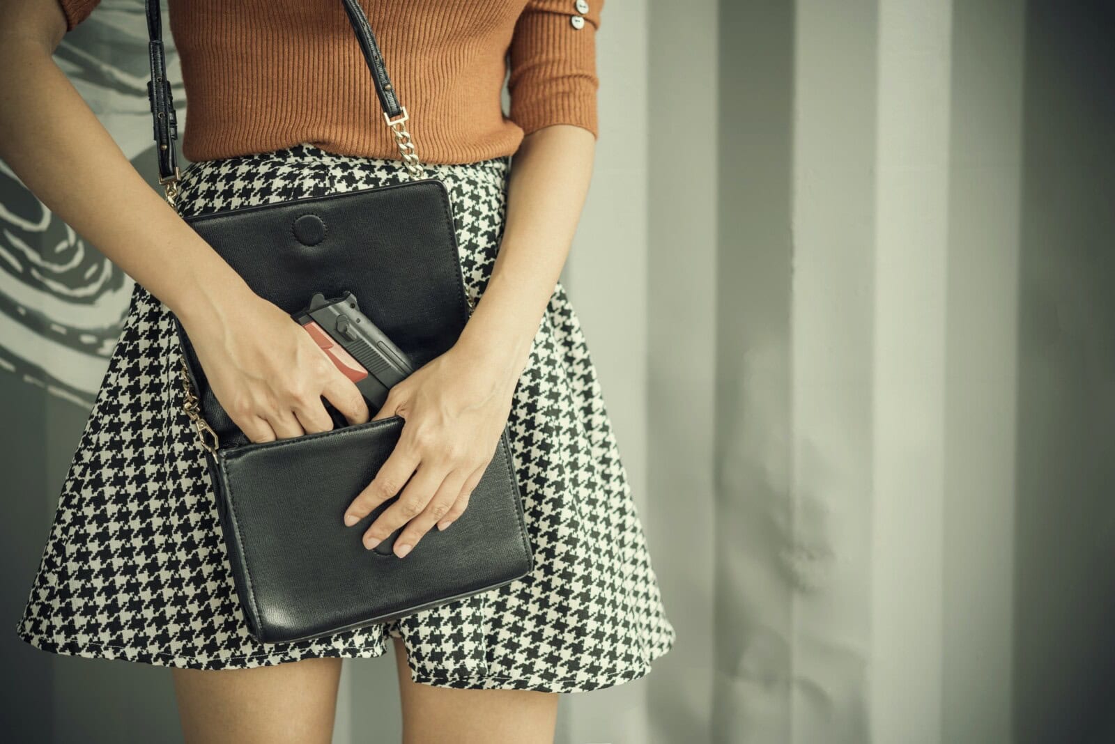 Photo of hand of young woman pulling a pistol out of her handbag with free copy space.