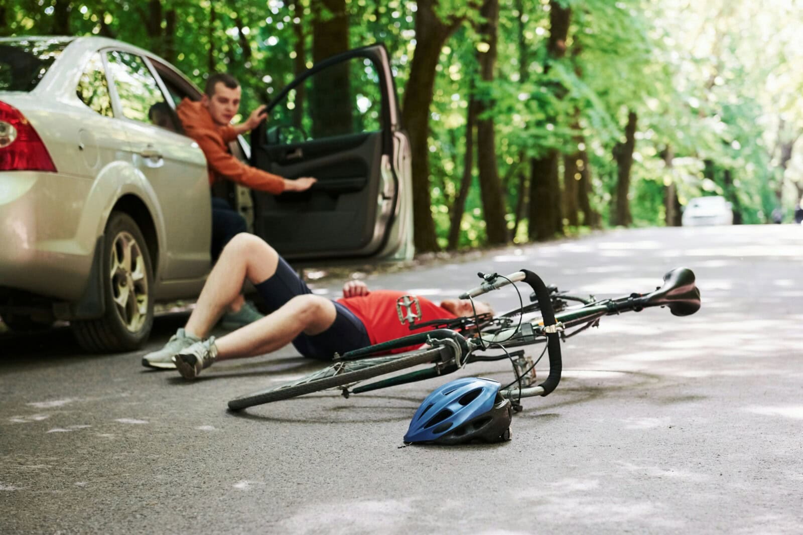 Victim on the asphalt. Bicycle and silver colored car accident on the road at forest at daytime