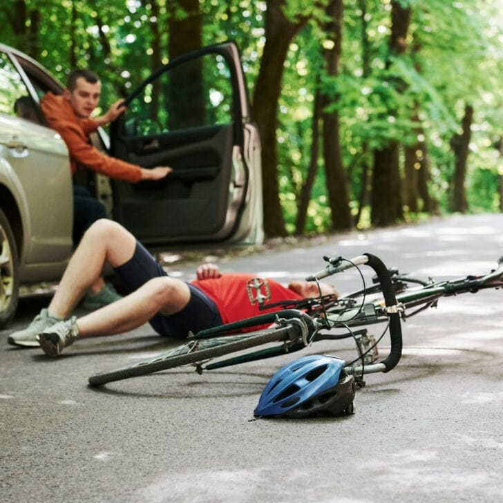 Victim on the asphalt. Bicycle and silver colored car accident on the road at forest at daytime