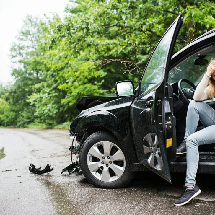 Young woman in the damaged car after a car accident, making a phone call.