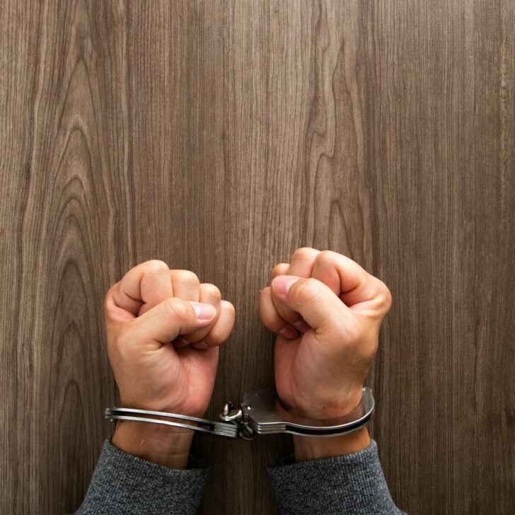 Arrested criminal hands locked in handcuffs.