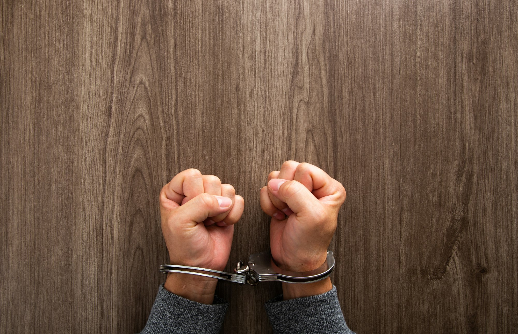 Arrested criminal hands locked in handcuffs.