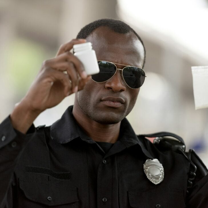 african american policeman holding drugs in plastic zipper and pills jar