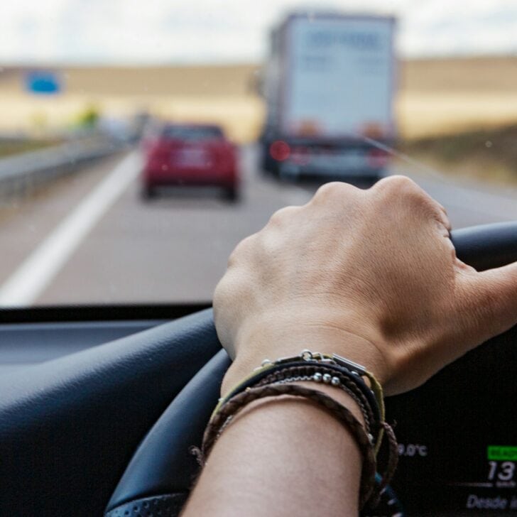 Female hand on the steering wheel driving a car in a highway, road trip on vacation