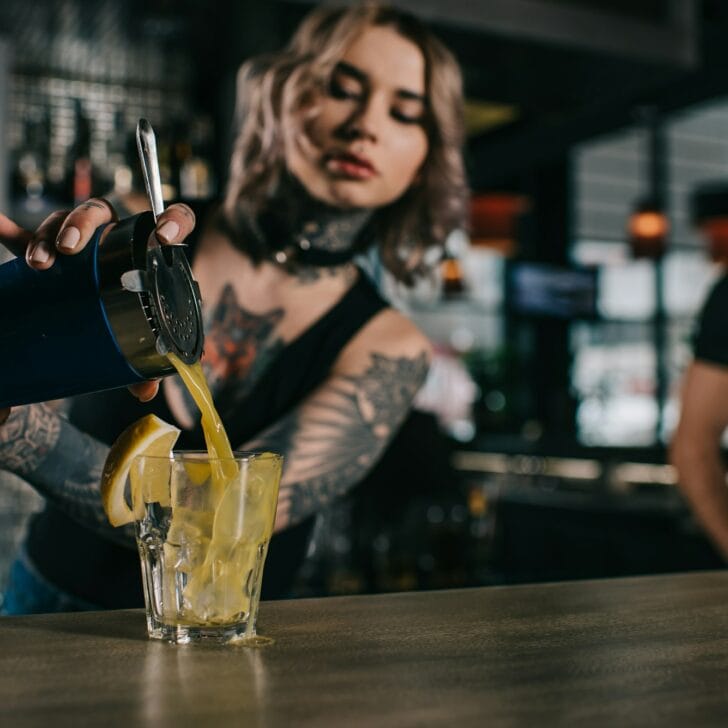 tattooed bartender preparing drink at bar
