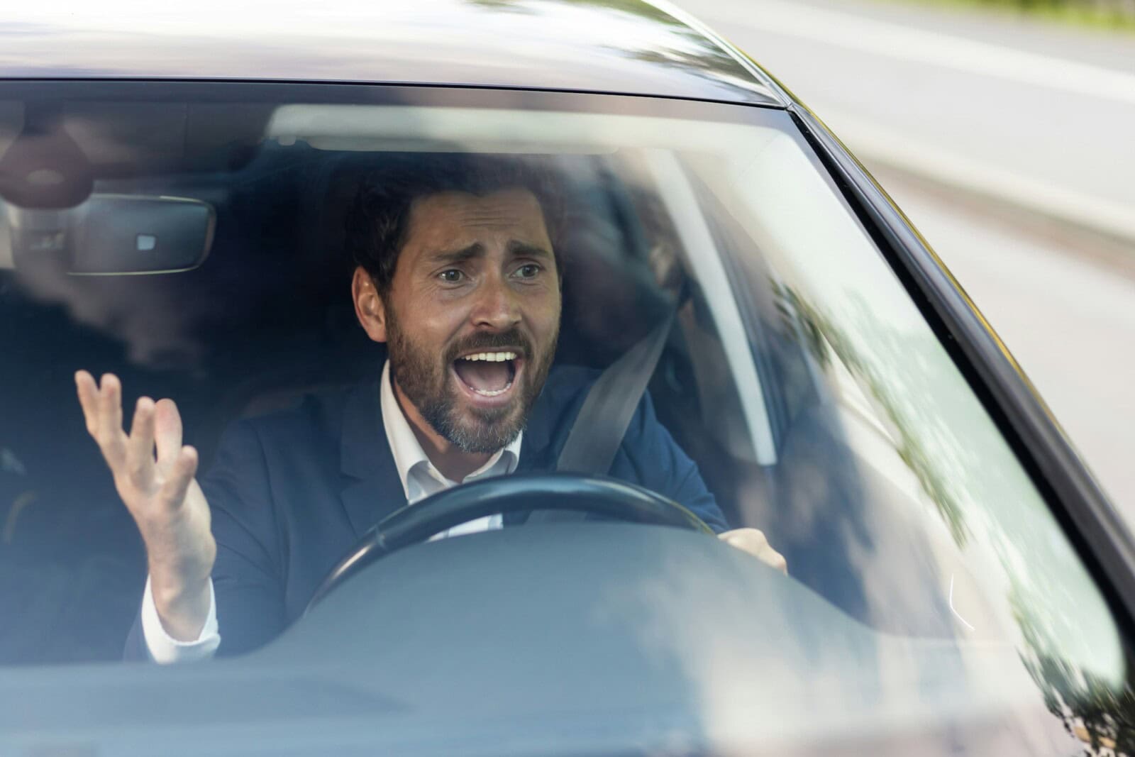 Angry male car driver yells at other drivers and pedestrians who obstruct traffic, mature adult