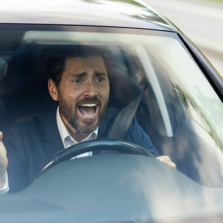 Angry male car driver yells at other drivers and pedestrians who obstruct traffic, mature adult