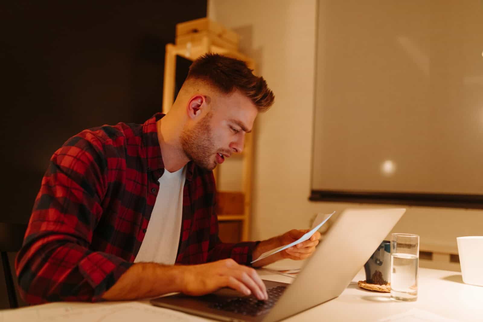 a young boy pays bills using a laptop. A young businessman works overtime from home.