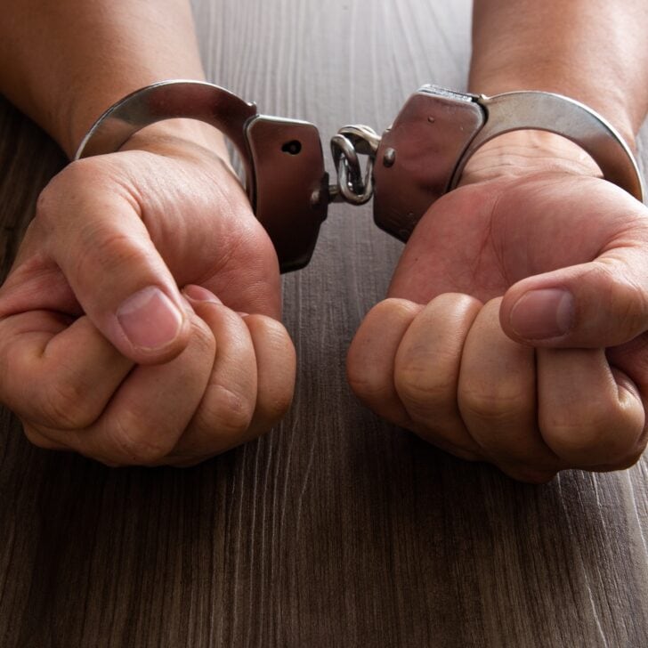 Arrested criminal hands locked in handcuffs.