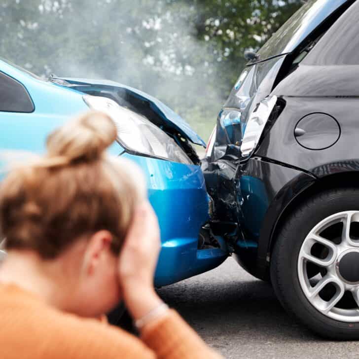 Female Motorist With Head In Hands Sitting Next To Vehicles Involved In Car Accident