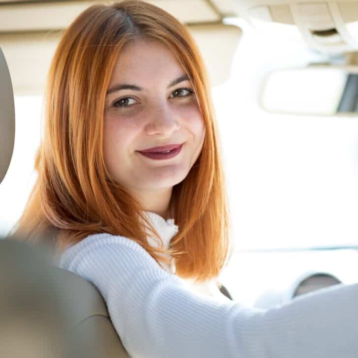 Young redhead woman driver driving a car smiling happily