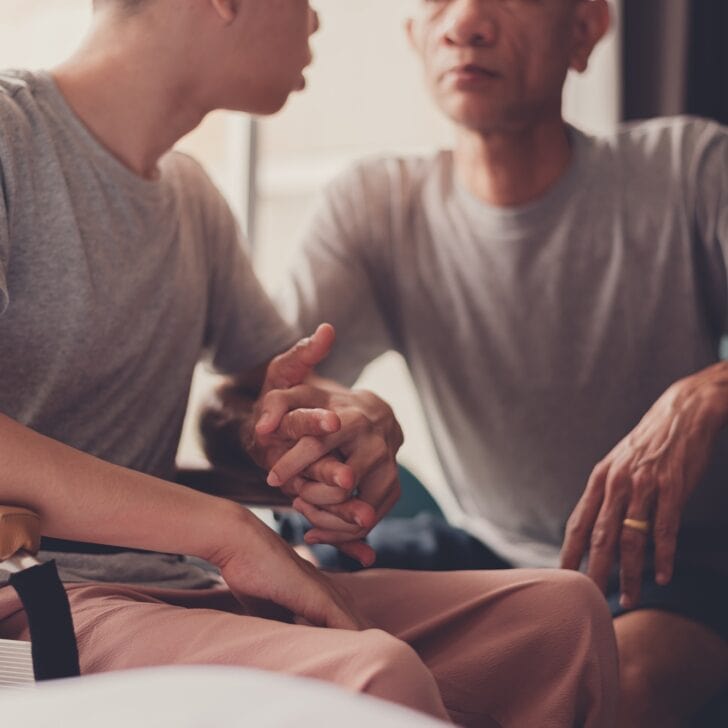 Hands of a young man with disability and father in the living room at home