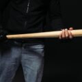 Cropped view of african american hooligan in glove holding baseball bat isolated on black