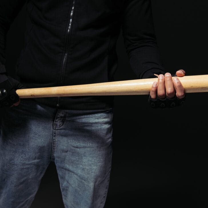 Cropped view of african american hooligan in glove holding baseball bat isolated on black