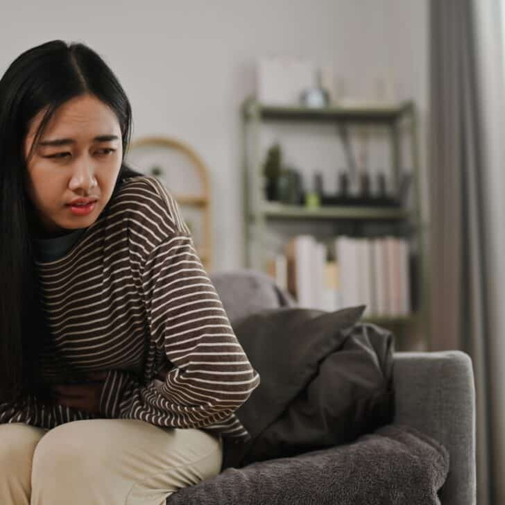 Young woman suffering from from period crumps or food poisoning, sitting on sofa at home
