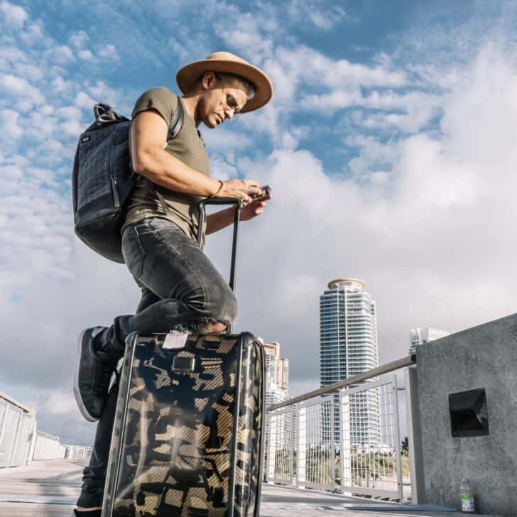 Traveller man texting phone with his luggage walking on Ocean drive South Beach Florida