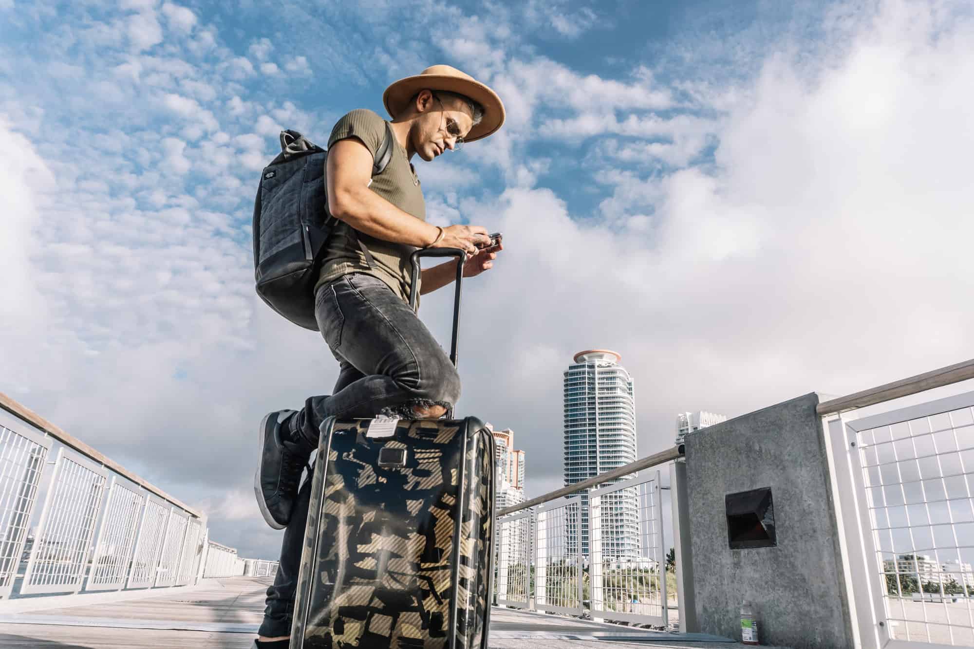 Traveller man texting phone with his luggage walking on Ocean drive South Beach Florida