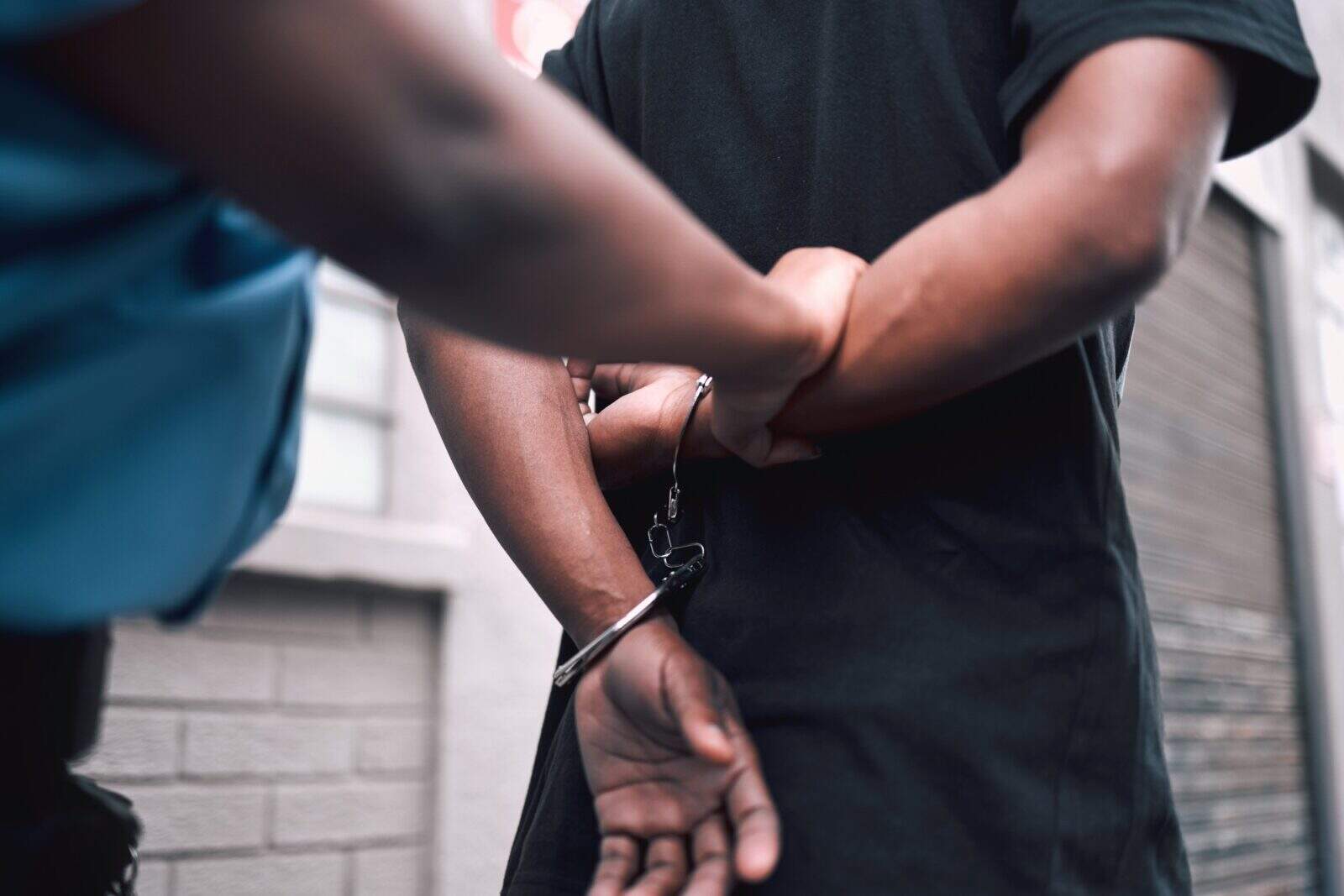 Hands, handcuffs or arrest with a police officer and criminal walking outdoor in a city from the ba